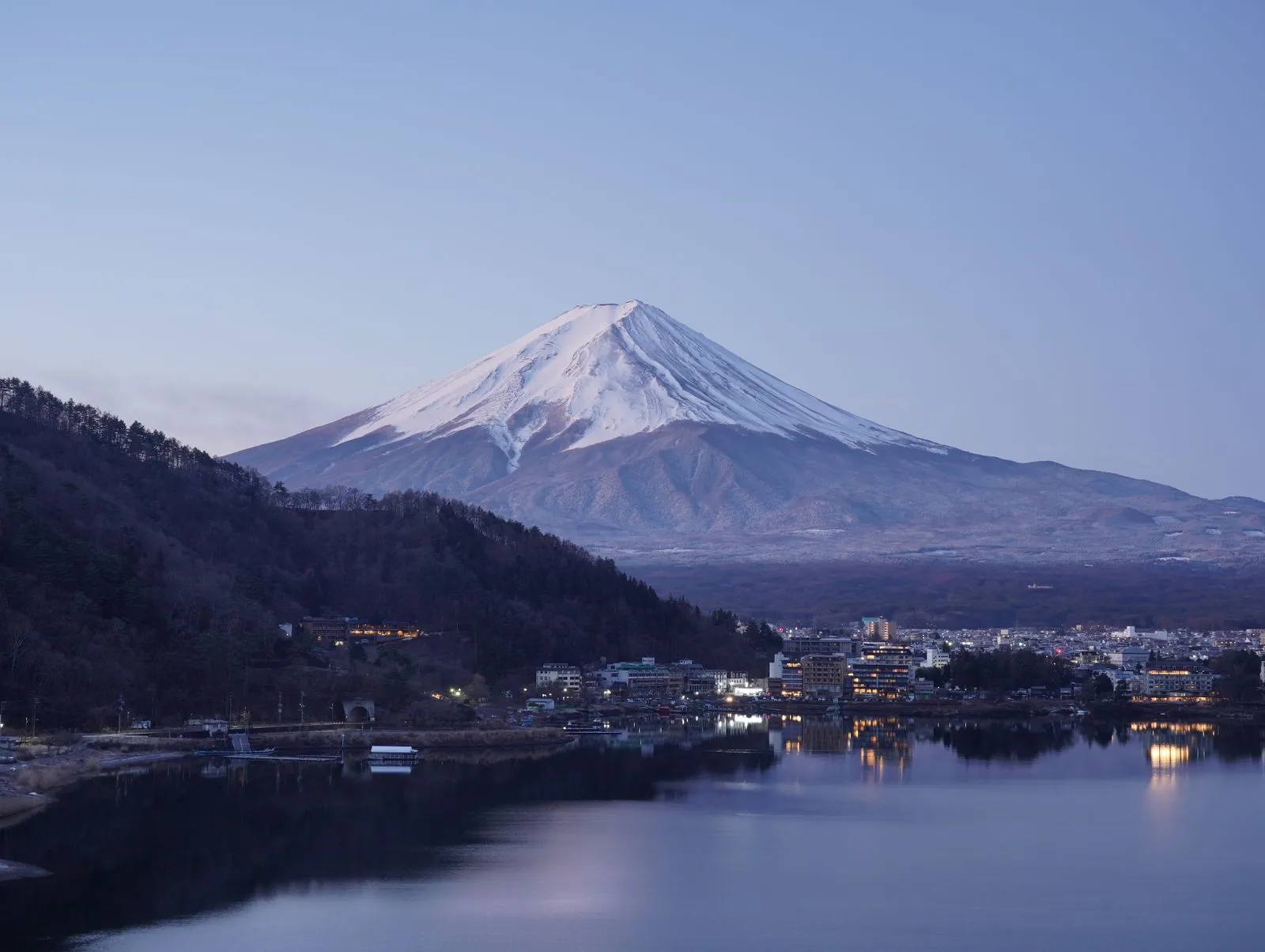 Snow-capped Mt Fuji at dusk above Lake Kawaguchi, lights coming on in the lakeside town