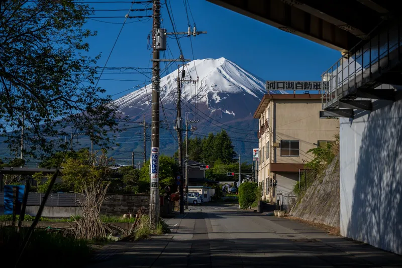 Town street lined with power lines leading toward snow-capped Mt Fuji