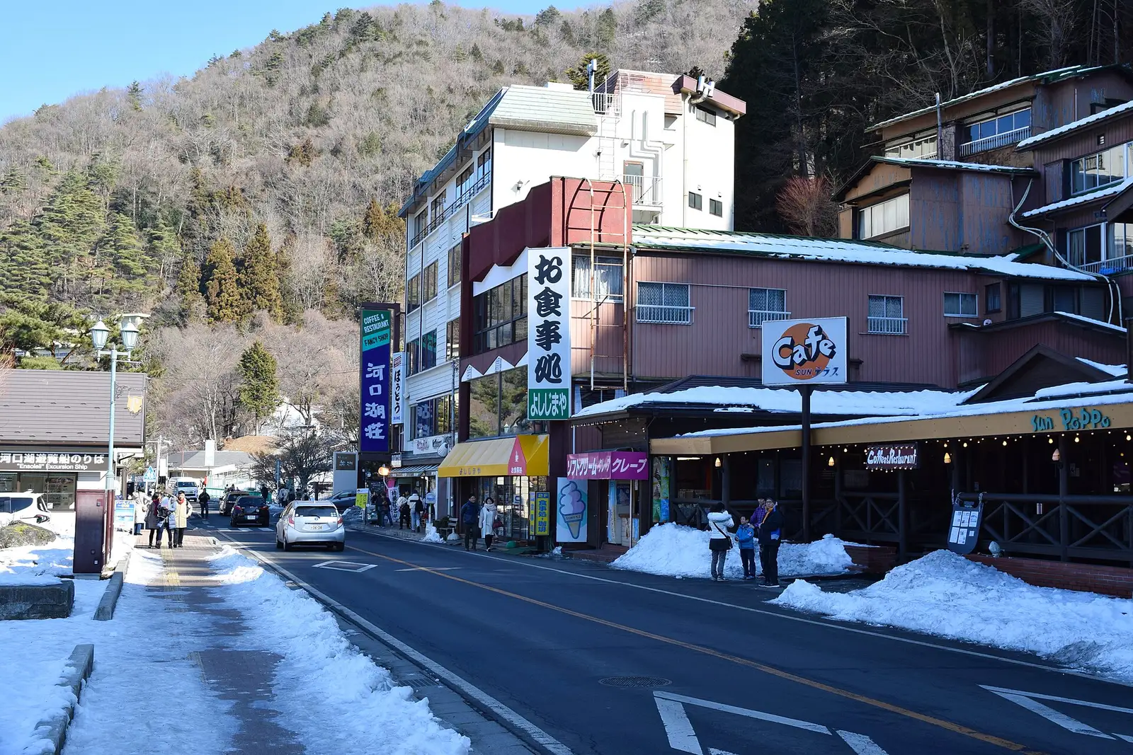Shops and cafés on a snowy street, wooded hill behind