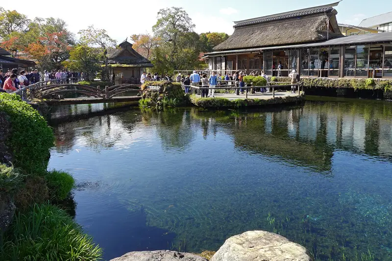 Spring pond at Oshino Hakkai with a wooden bridge and thatched house, autumn trees