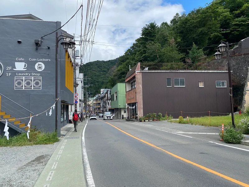 Street into Kawaguchiko town past a café and laundry, forested hill behind