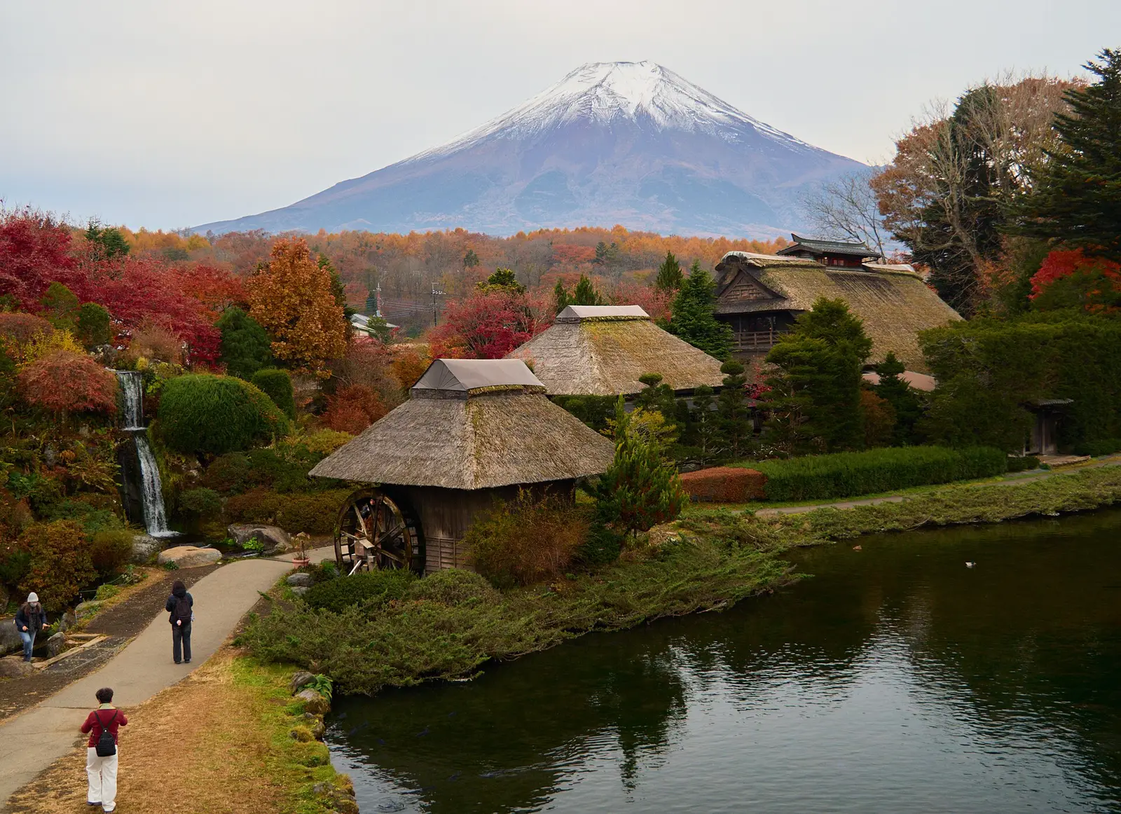 Mt Fuji above thatched houses, a water wheel and a pond in autumn colour at Oshino Hakkai