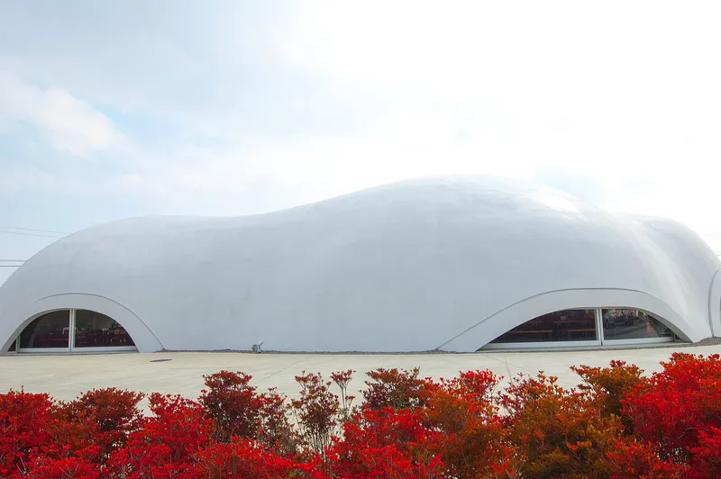 The white dome building of a Hoto Fudo noodle restaurant behind red azaleas