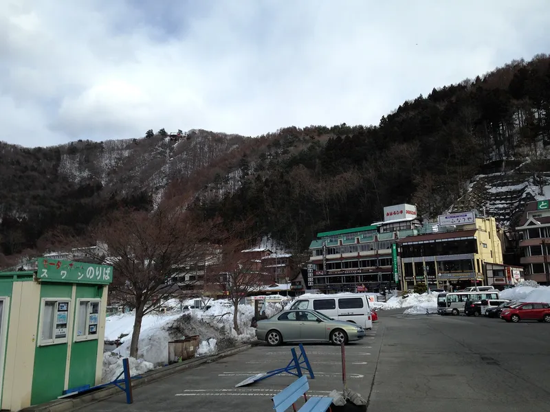 Lakeside car park and swan-boat kiosk below a snowy wooded hill