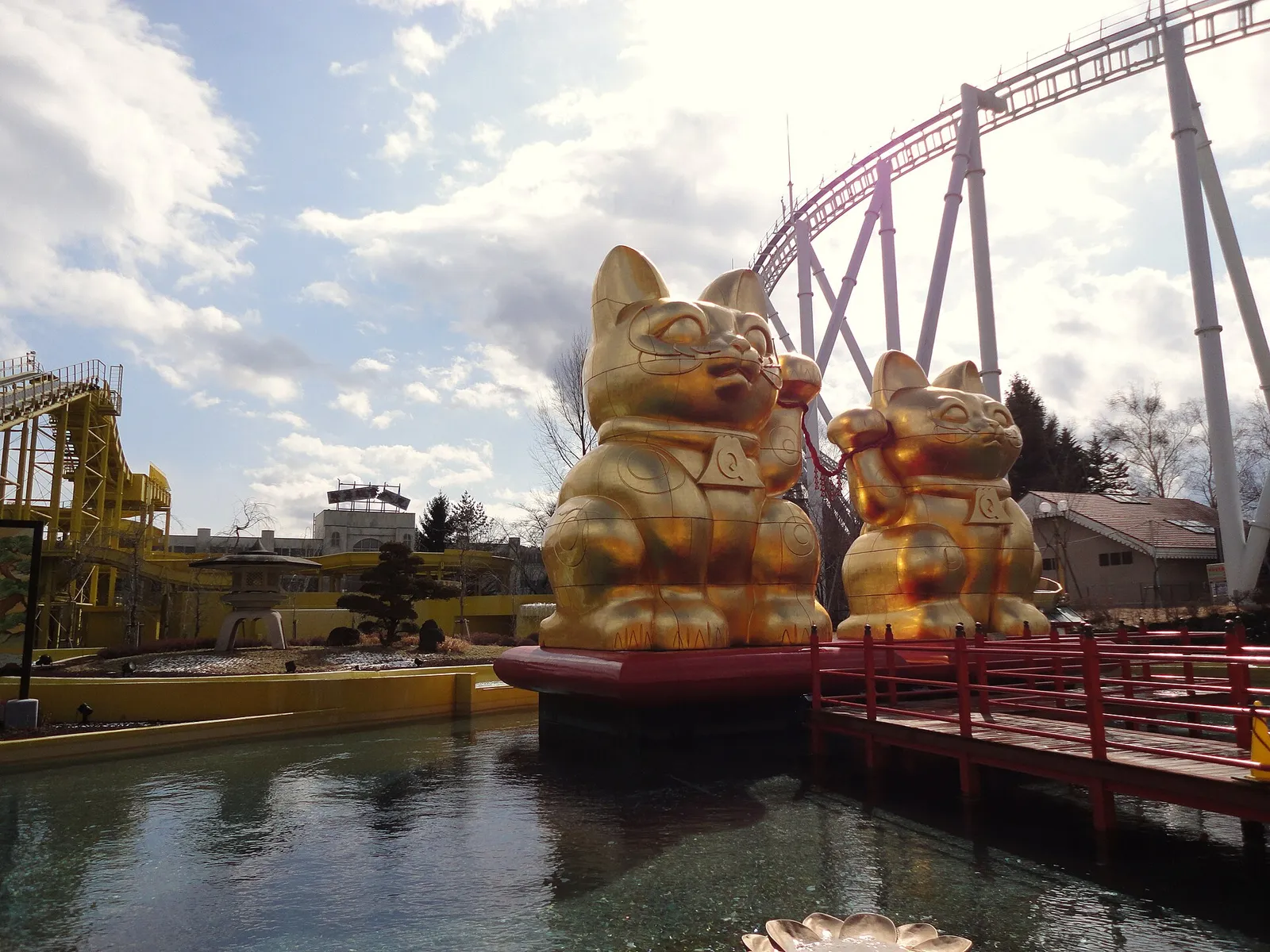 Two giant golden lucky-cat statues on a pond under a roller coaster at Fuji-Q Highland