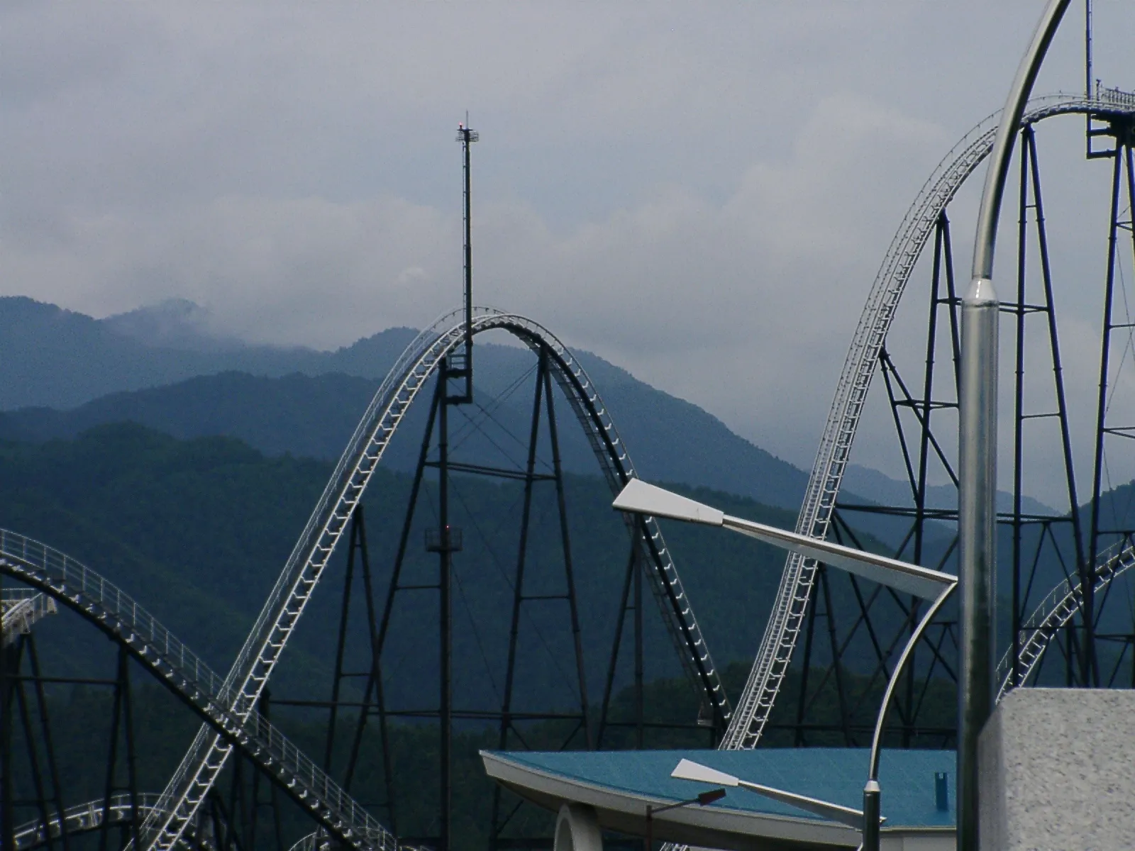 Tall roller coaster tracks against green mountains at Fuji-Q Highland on a cloudy day