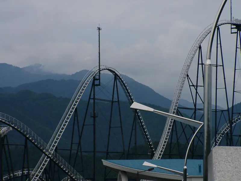 Tall roller coaster tracks against green mountains at Fuji-Q Highland on a cloudy day