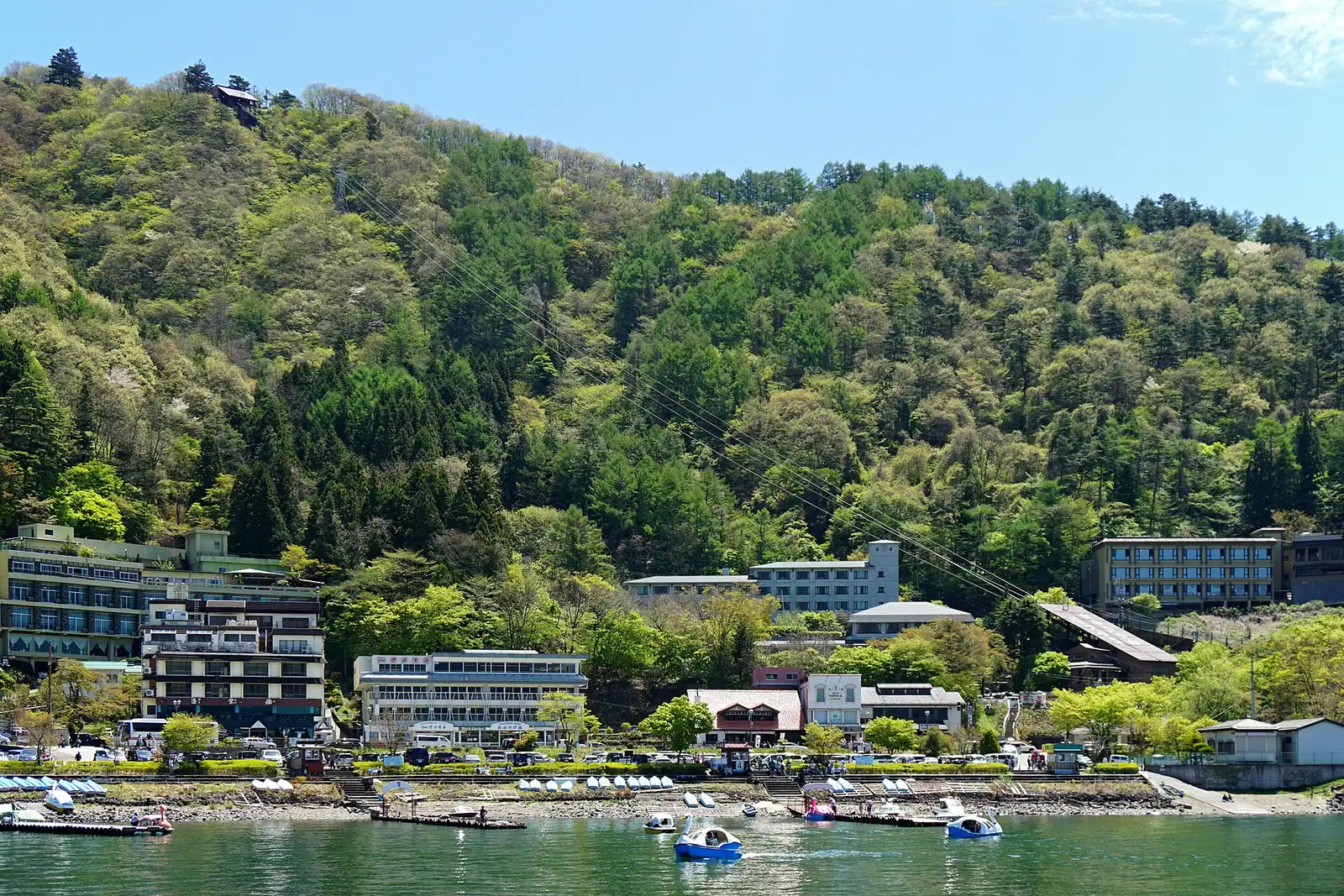 Lakeside hotels below Mt Tenjo with the ropeway cables up the slope, swan boats on Lake Kawaguchi