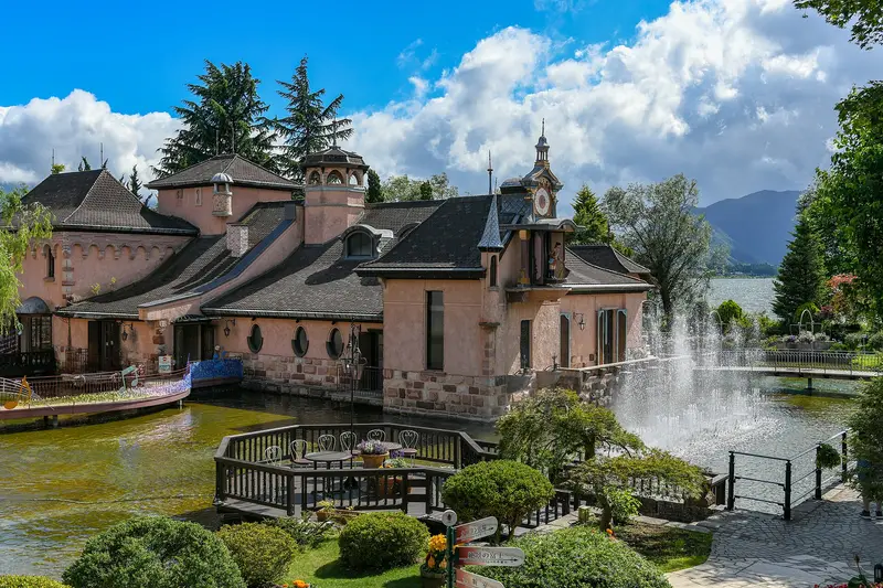 Pink European-style buildings by a pond with a fountain, Lake Kawaguchi behind