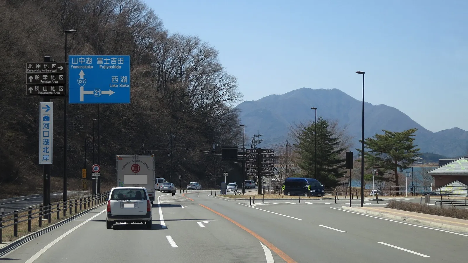 Main road with signs for Lake Saiko and Fujiyoshida, a mountain ahead