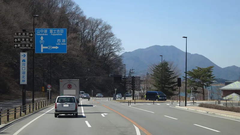 Main road with signs for Lake Saiko and Fujiyoshida, a mountain ahead