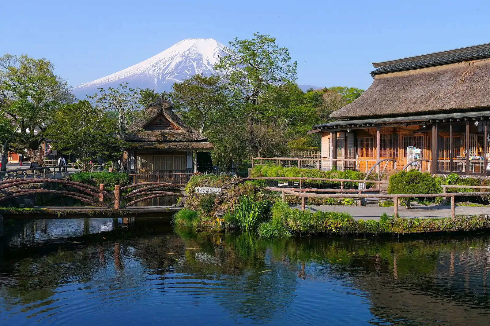 Snow-capped Mt Fuji above thatched houses and the spring pond at Oshino Hakkai